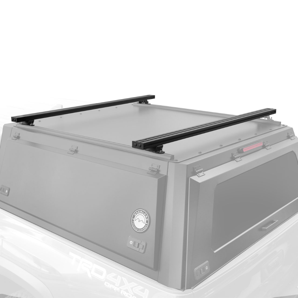 Heavy-duty black aluminum truck cap crossbars mounted on vehicle roof with mounting points for overland gear