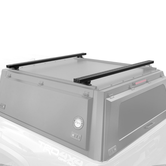 Heavy-duty black aluminum truck cap crossbars mounted on vehicle roof with mounting points for overland gear