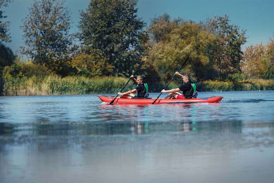 Two people paddling a red kayak on a calm lake with trees in the background