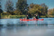 Two people paddling a red kayak on a calm lake with trees in the background