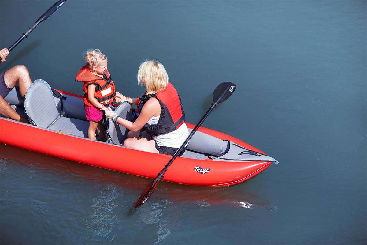 Two people in a red kayak on calm water with a paddle.