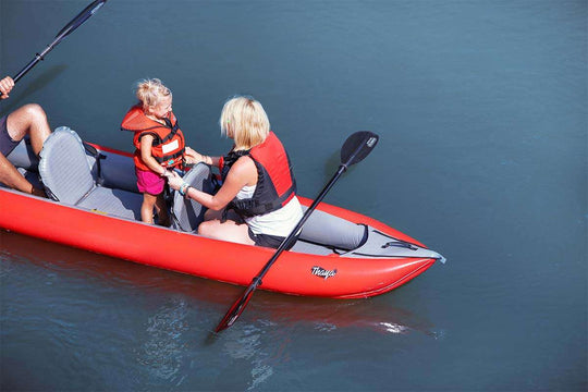 Two people in a red kayak on calm water with a paddle.