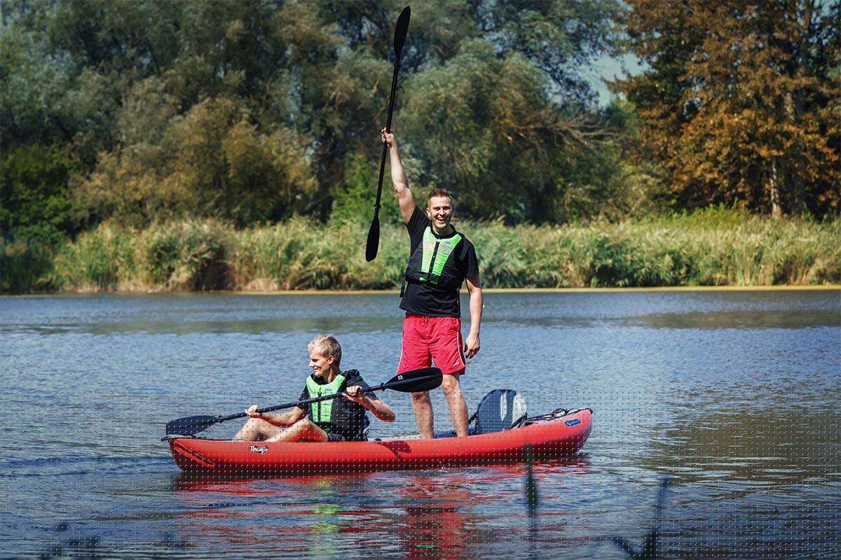 Two people in a kayak on a calm lake with trees in the background
